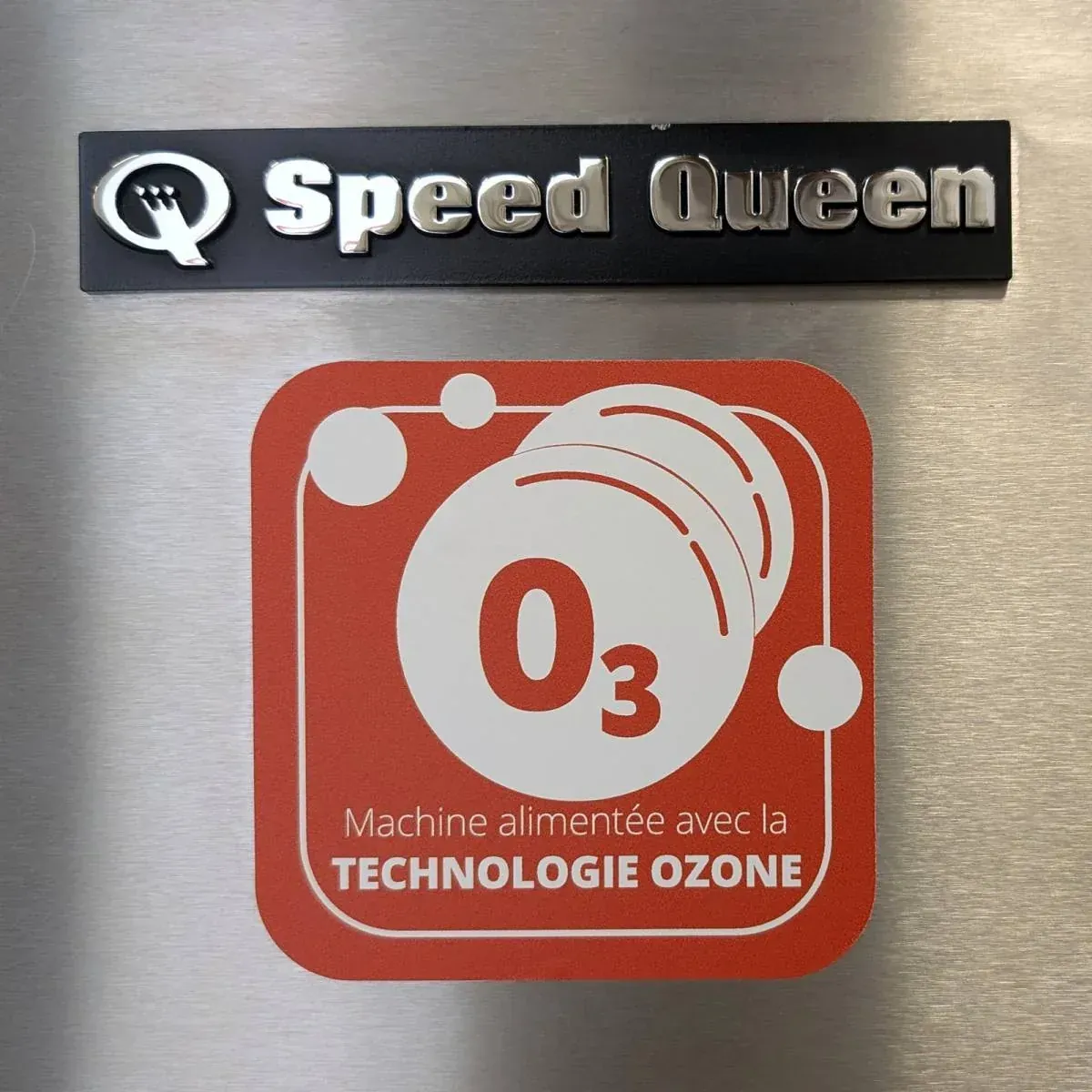 The Speed Queen plate and the red “machine running on ozone technology” badge on the stainless steel side of a washing machine